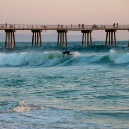 Surfer riding waves near wooden pier at sunset, representing coastal Los Angeles destination