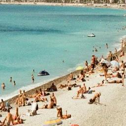 Crowded beach scene with turquoise Mediterranean waters and sunbathers on golden sand in Nice