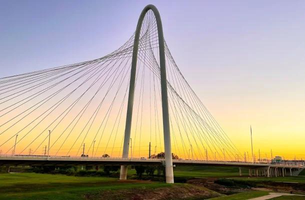 Modern cable-stayed bridge with twin arches spanning across Dallas skyline during golden sunset