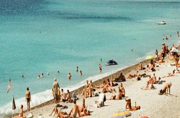 Crowded beach in Nice with sunbathers on white sand and turquoise Mediterranean waters