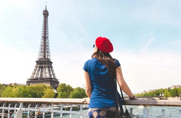 Woman in red beret admiring Eiffel Tower from Seine riverbank on sunny day in Paris