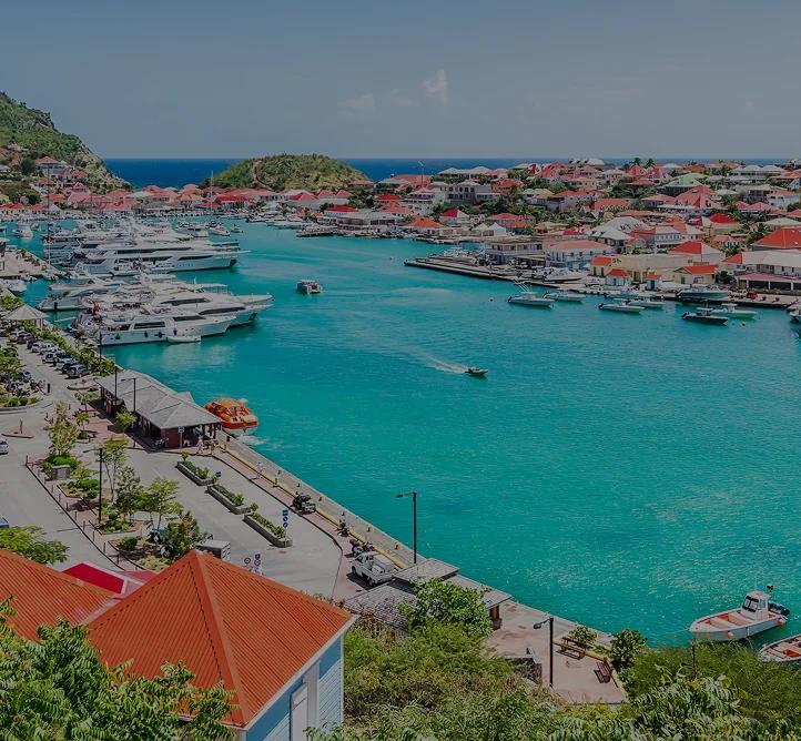 Stunning aerial view of St. Barts harbor with luxury yachts, red-roofed villas, and turquoise waters