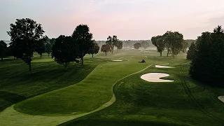 Pristine golf course at dawn with rolling fairways, sand bunkers, and morning mist over greens