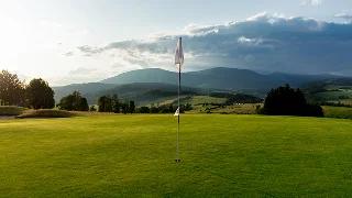 Pristine golf course with flagstick on manicured green fairway, mountain ranges visible in distance