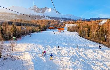 Snow-covered ski slopes with chairlift and skiers at Aspen mountain resort under clear blue skies