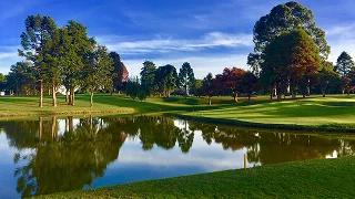 Pristine golf course with water hazard reflecting autumn trees under blue sky in Palm Beach area