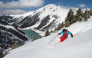Skier carving fresh powder down snowy mountain slopes with dramatic alpine peaks and valley views