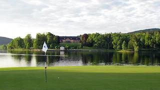 Pristine golf green with flag overlooking serene lake and forested hills at Pinehurst resort