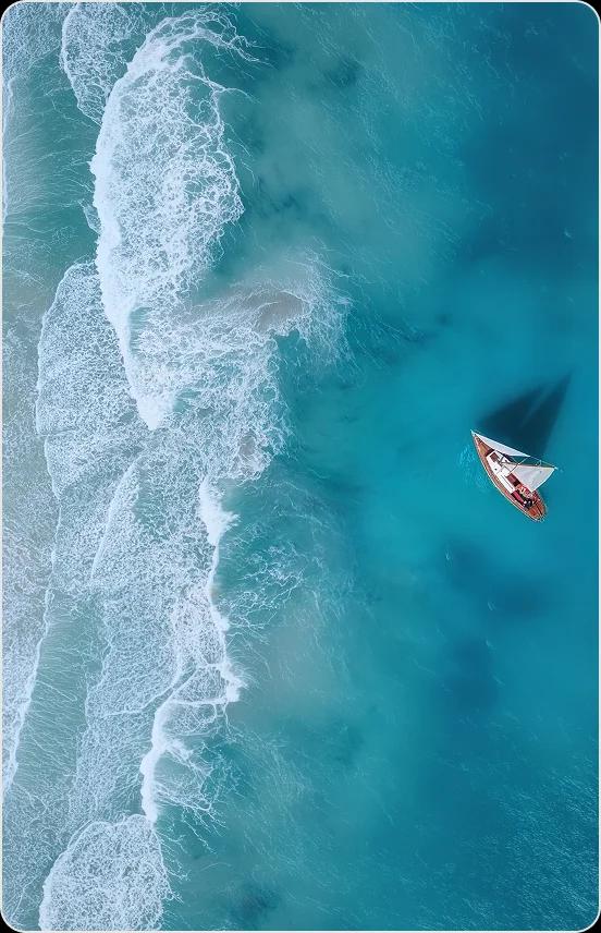 Aerial view of turquoise ocean waters with white foam waves meeting pristine coastline and small boat