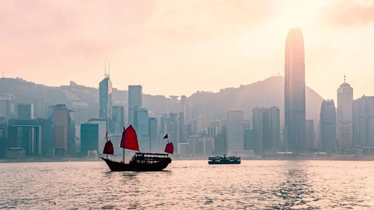 Traditional red-sailed junk boat sailing past Hong Kong's iconic skyline at golden hour sunset